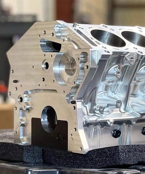 CNC machined billet aluminum engine block showing cylinder bores, cooling jackets, and complex external milling details.