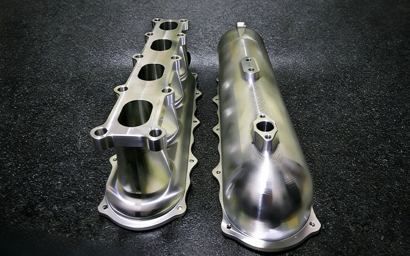 Custom billet aluminum intake manifold with CNC machined plenum and runners for high-performance engines.