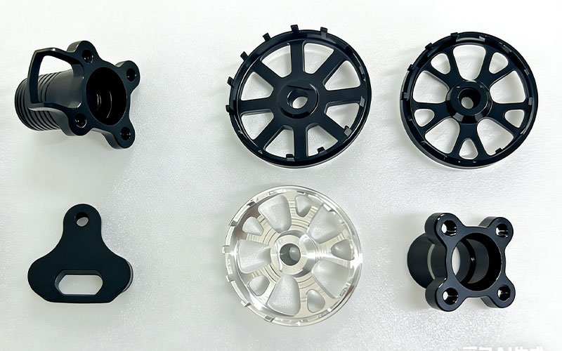 Set of custom CNC machined aluminum drone parts including black anodized motor mounts with cooling fins and lightweight wheel guards.