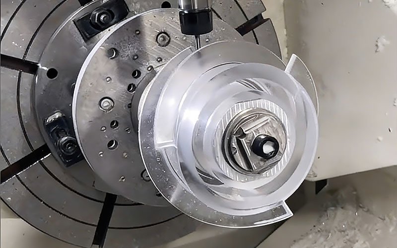 5-axis CNC machining center milling a complex spiral acrylic component held in a rotary fixture.