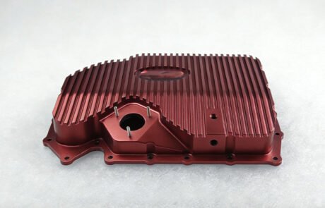 Custom CNC machined billet aluminum oil pan with integrated cooling fins and red anodized finish.