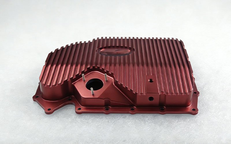 Custom CNC machined billet aluminum oil pan with integrated cooling fins and red anodized finish.