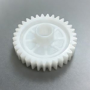 Precision CNC machined white Delrin (Acetal) spur gear with a central hub and lightweight spoke design, used for mechanical power transmission.