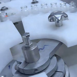 Custom CNC machined Delrin star wheel and guide plates handling glass vials on a high-speed pharmaceutical filling machine.