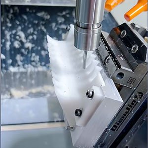 Close-up of a CNC milling machine cutting a complex white plastic electrical insulator with slotted geometry for the electronics industry.