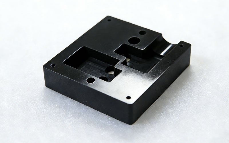 Custom component manufactured via Black POM CNC machining featuring milled pockets and drilled holes.