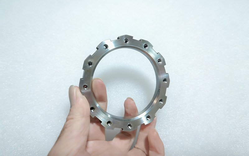 Hand holding a finished CNC machined titanium Ti-6Al-4V locking ring to demonstrate surface finish and scale.