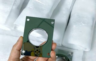 A custom high-gloss aluminum component, precision machined to a mirror-like finish, held against a background of protective foam packaging. The part features a central circular cutout and mounting holes, showcasing the smooth, reflective surface achievable through advanced CNC high-gloss cutting.