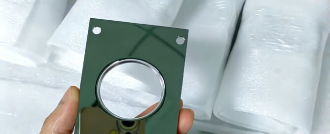 A custom high-gloss aluminum component, precision machined to a mirror-like finish, held against a background of protective foam packaging. The part features a central circular cutout and mounting holes, showcasing the smooth, reflective surface achievable through advanced CNC high-gloss cutting.