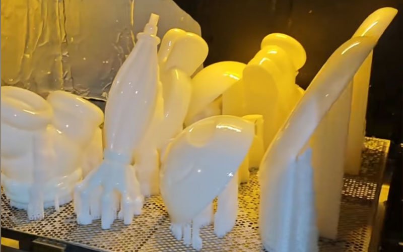 Batch of white SLA resin 3D printed parts on the build platform, featuring support structures and complex curved shapes.