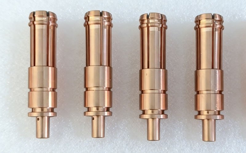 Four precision CNC turned copper connector terminals for EV applications, featuring longitudinal slits and a bright finish.