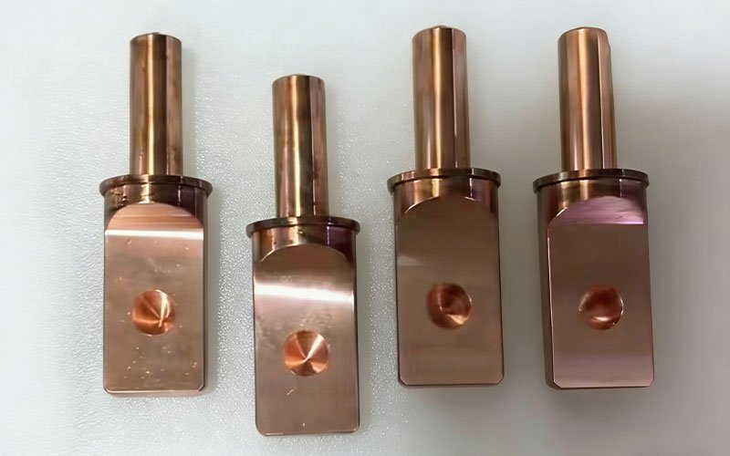 Four precision CNC machined copper alloy terminals with flat contact surfaces and cylindrical posts for high-current EV power distribution.