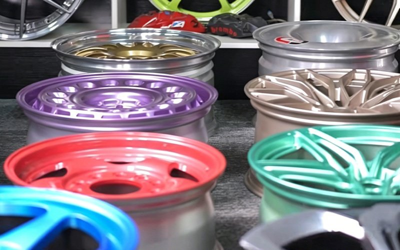 A diverse collection of finished custom CNC forged wheels showcasing various premium surface treatments, including vibrant powder coats and anodized finishes in purple, red, blue, green, and gold.