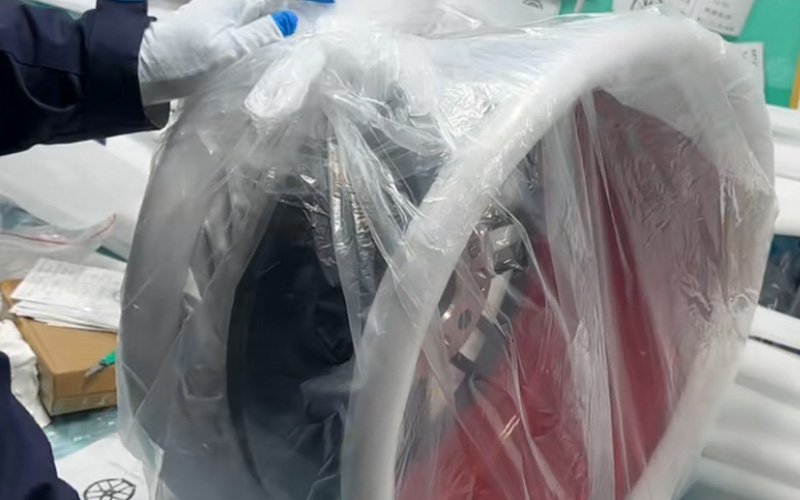 A staff member wearing white gloves is carefully wrapping the finished custom forged wheel in protective plastic and thick foam edge protectors to ensure safe global shipping.
