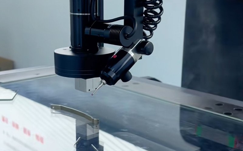 Close-up of a 2D profile projector contact probe positioned above a flat metal workpiece on the measurement table