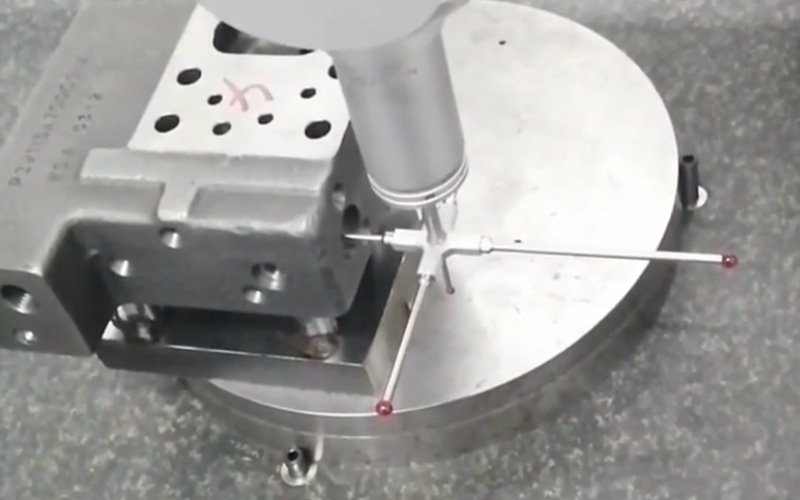 Overhead view of a CMM star-configuration touch probe measuring a complex aluminum machined part on the measurement table