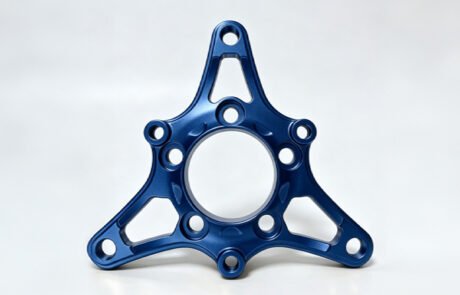 Custom CNC machined aluminum flange plate with a blue anodized finish, tri-arm design and central register bore