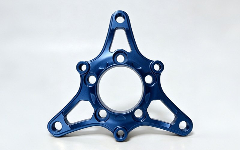 Custom CNC machined aluminum flange plate with a blue anodized finish, tri-arm design and central register bore