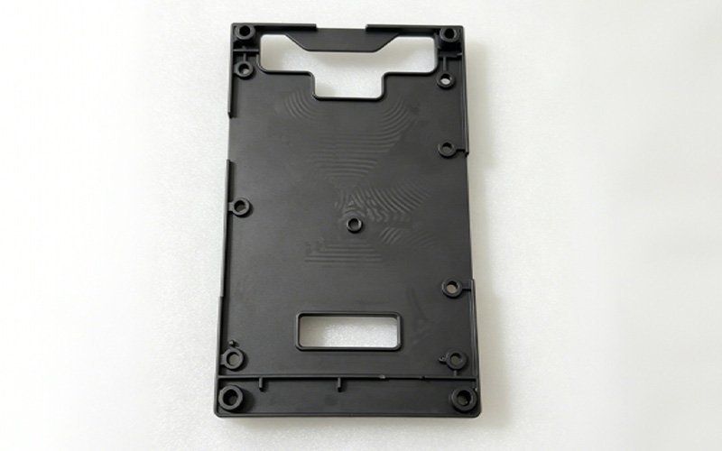 Custom GF30 nylon machining case — thin black mounting plate with screw bosses, shaped cutout, and rectangular window, machined from solid