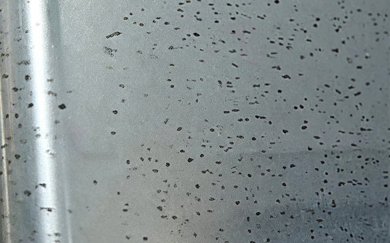 Close-up of anodized 7075 aluminum surface covered in scattered black spots and pitting