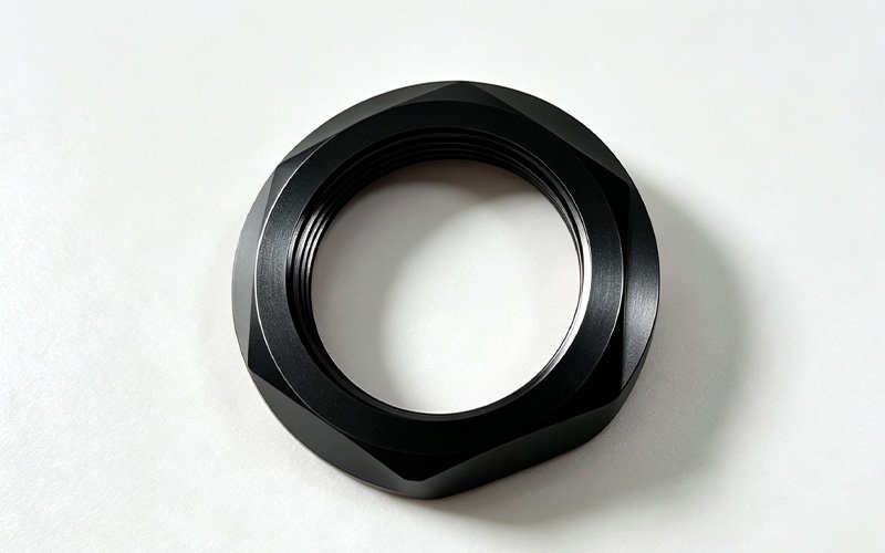 Custom CNC machined anti-slip lock nut in black anodized aluminum with faceted grip profile and anti-slip face teeth