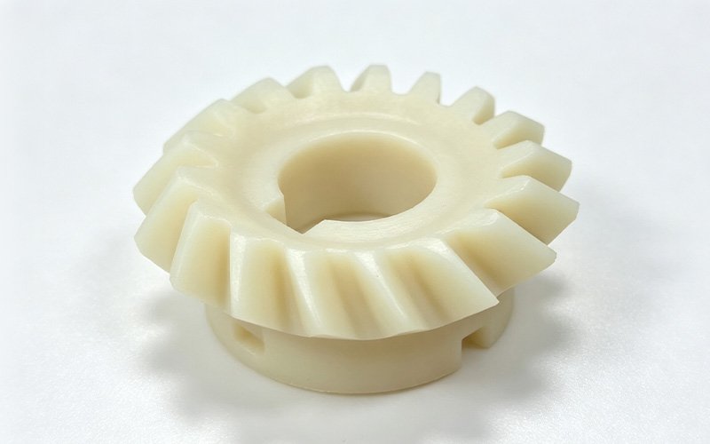 Custom CNC machined natural PEEK bevel gear with angled teeth, a keyed center bore and a hub