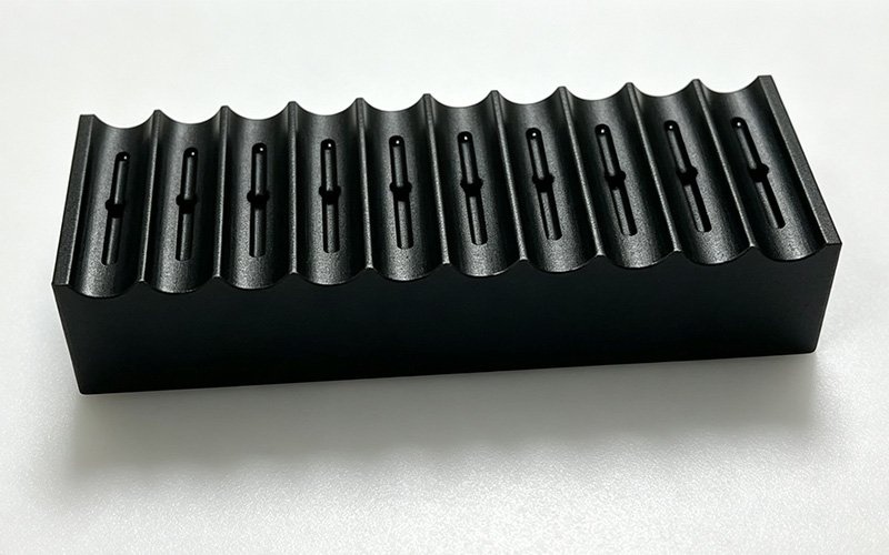 Custom CNC machined Delrin fixture for automation equipment with a row of curved locating channels and clearance slots