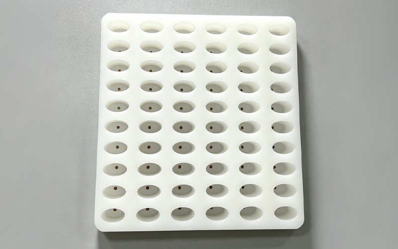 Custom CNC machined white Delrin locating tray for automation with a grid of tapered pockets and bottom holes